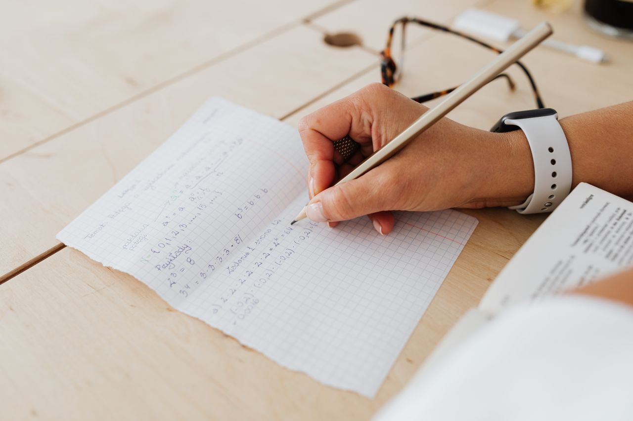 Home A close-up of a person writing mathematical equations on graph paper with a pencil.