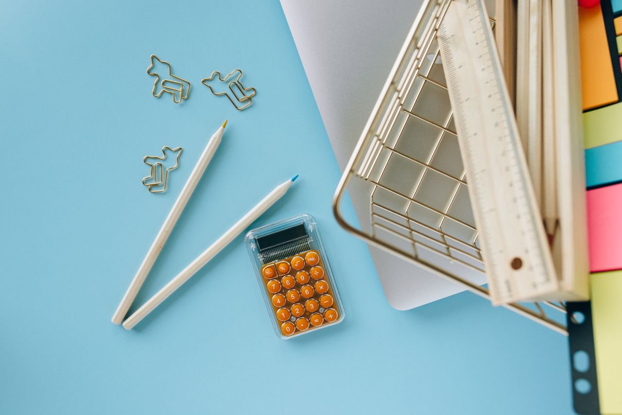 Top view of a modern workspace featuring pencils, calculator, and vibrant sticky notes on a blue background.